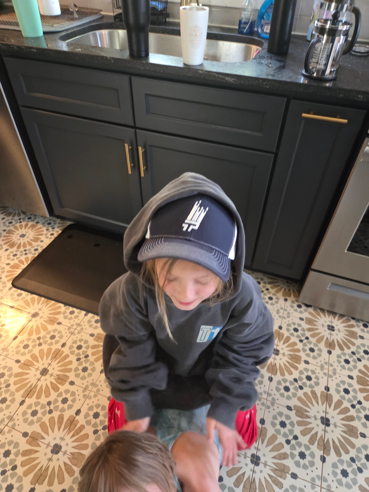 A child wearing a That 1 Painter cap and hoodie at home.