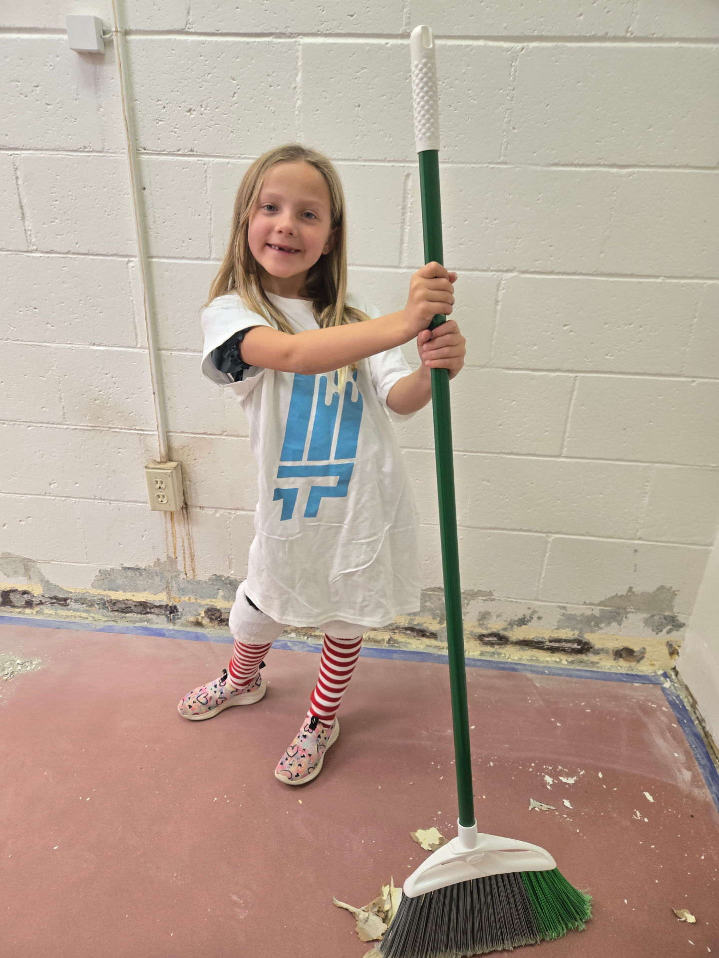 A child in a That 1 Painter shirt holding a broom, showing the family side of the business.